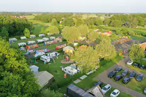 Campingplatz aus der Vogelperspektive: Stellplätze mit Wohnmobilen und Wohnwagen, Bäume, Wege und ein Spielbereich im Grünen.