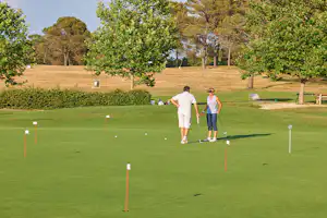 Zwei Personen gehen auf einem gepflegten Golfplatz zwischen Bäumen, mit Abschlagpfosten und Fahnen im Vordergrund.
