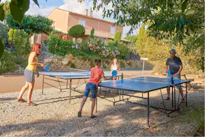 Tischtennisplatte auf dem Campingplatz vor einem Steingarten und einem Wohngebäude mit Terrasse und Bäumen.