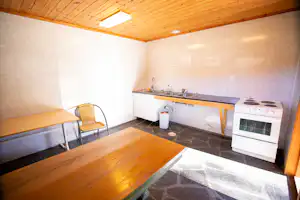 Innenraum einer Sauna mit Holzdecke, Bank, Steinboden und Ofen mit Herdplatte an der Wand.