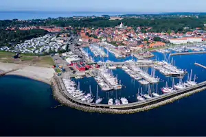 Luftaufnahme eines Hafens mit vielen Segelbooten, Stegen und Wellenbrechern am Ufer, dahinter ein Campingplatz mit Wohnwagen.