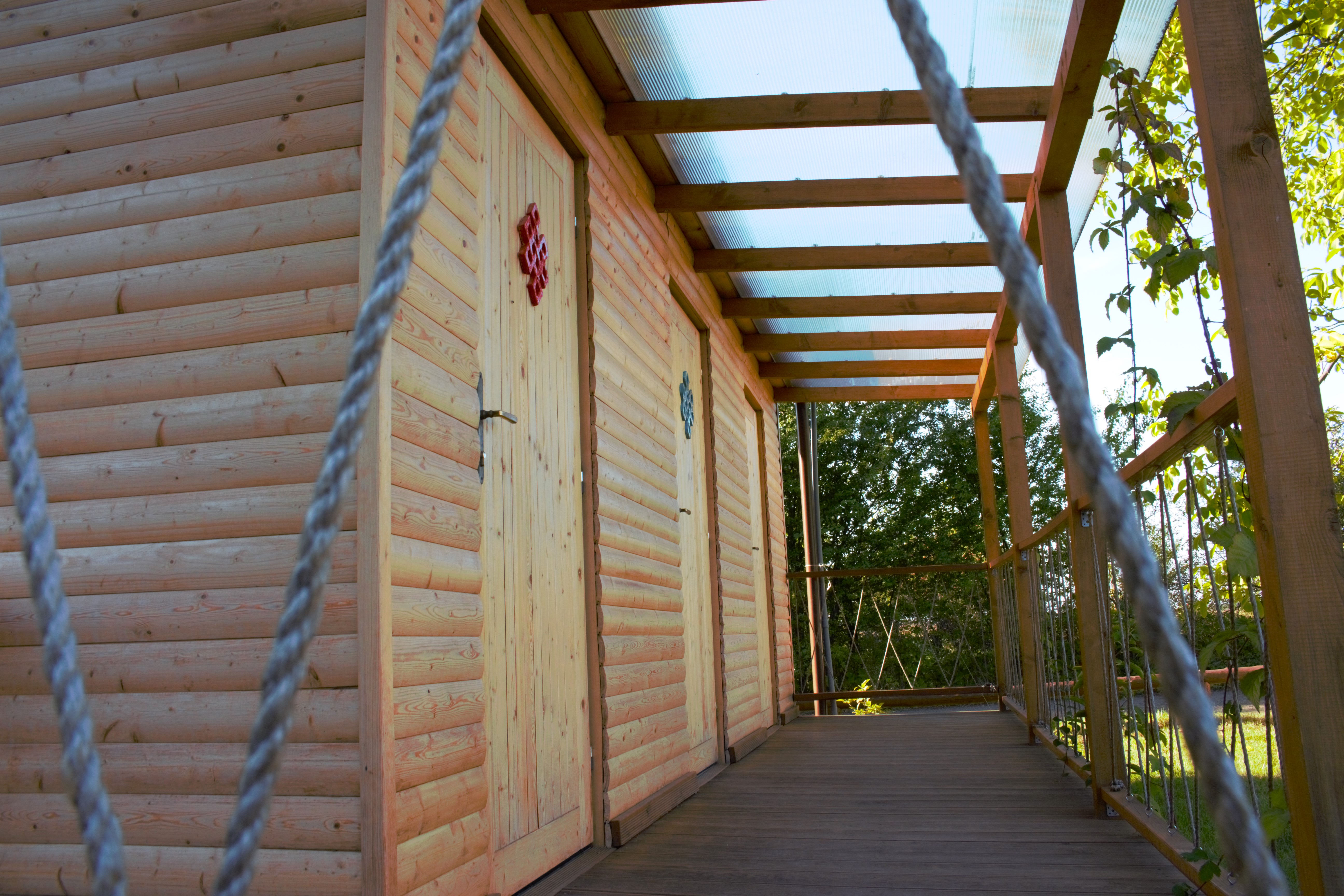 Holzbungalow mit Veranda aus Holz, Seil vor der Fassade und Blick auf den Weg zwischen den Wänden und Bäumen.