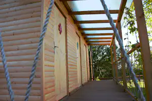 Holzbungalow mit Veranda aus Holz, Seil vor der Fassade und Blick auf den Weg zwischen den Wänden und Bäumen.