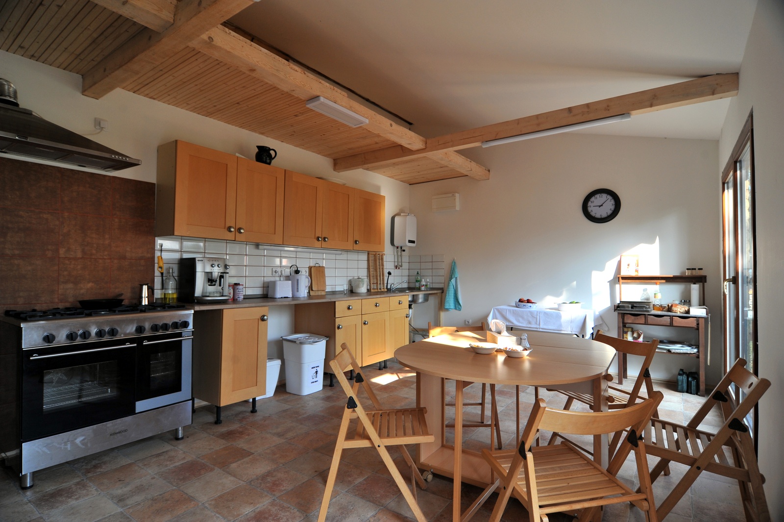 Wohnküche in einem Campinghaus mit Holzdecken, Küchenzeile, Backofen, Esstisch und Stühlen im Innenraum.