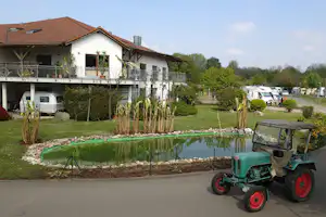 Grüner Traktor auf dem Weg vor einem Campingplatz mit Wohngebäuden, Balkonen und geparkten Wohnwagen