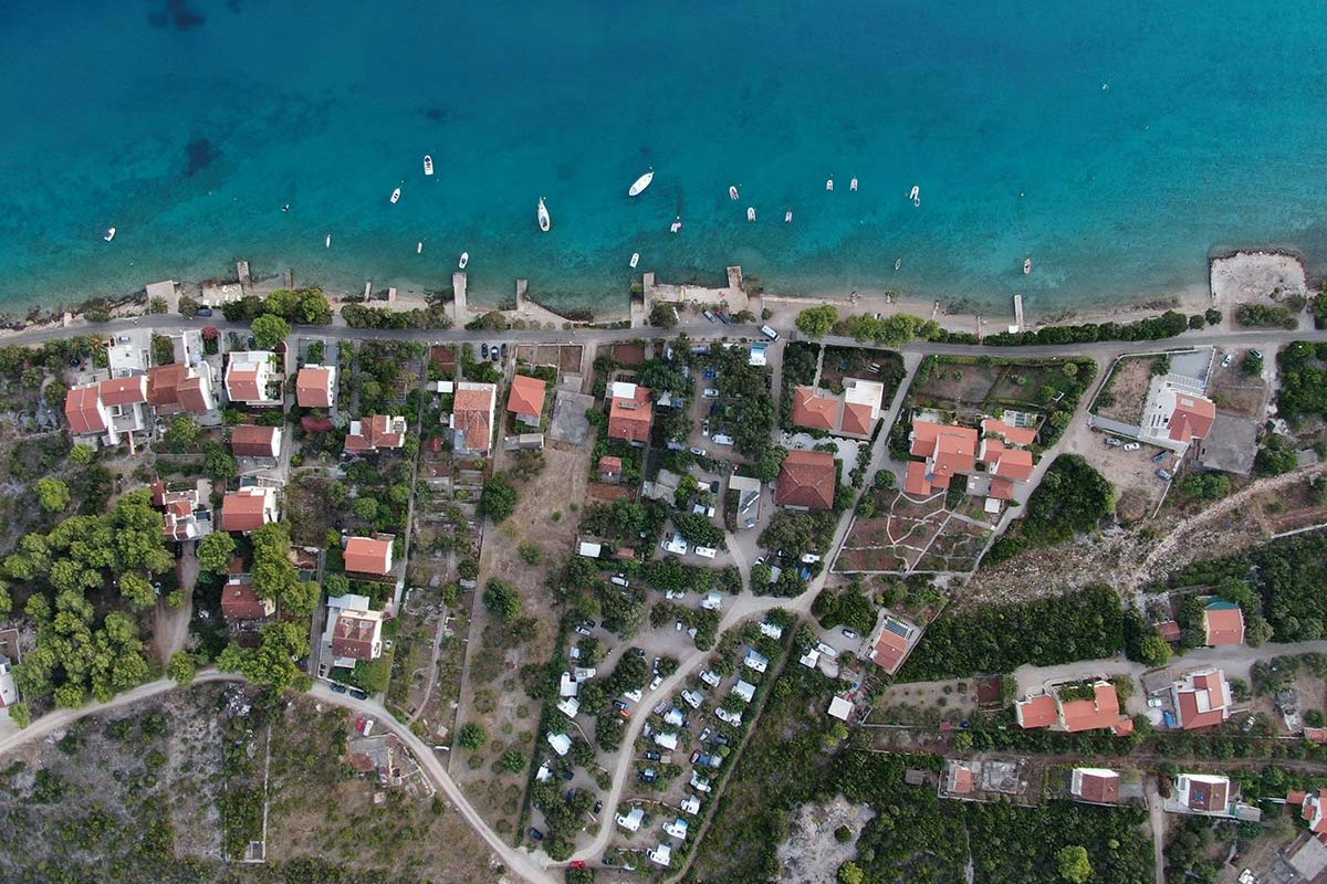 Luftaufnahme eines Campingplatzes mit vielen Stellplätzen, roten Dächern und Wegen, umgeben von Bäumen und Wasser.