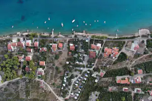 Luftaufnahme eines Campingplatzes mit vielen Stellplätzen, roten Dächern und Wegen, umgeben von Bäumen und Wasser.