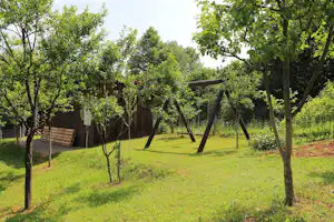 Spielplatz auf dem Campingplatz: Schaukel und Rutsche im grünen Garten mit Bäumen und Holzsichtschutzzaun.