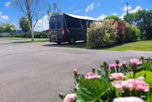 Wohnmobil auf einem Stellplatz am Campingplatz, im Vordergrund blühende Blumen und Sträucher, Asphaltweg und Bäume im Hintergrund.