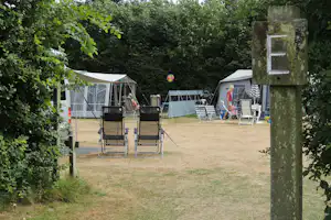 Campingzelte auf einem Grasplatz, davor Klappstühle und Sonnenschirm, im Hintergrund weitere Zelte im Grünen.