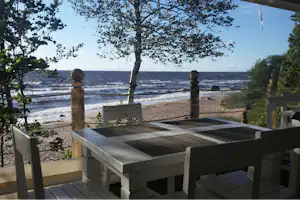 Terrasse mit Liegen und Blick auf das Meer, Strand und Wellen zwischen Bäumen und Holzgeländer.