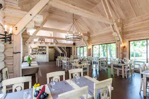 Innenansicht einer Holz-Gaststube mit Esstischen, Kerzenleuchtern, Kronleuchter und Barbereich mit Getränken.