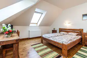 Doppelbett im Dachgeschoss mit Holzrahmen, gemusterten Bettdecken, Dachfenster und Heizkörper an der Wand.