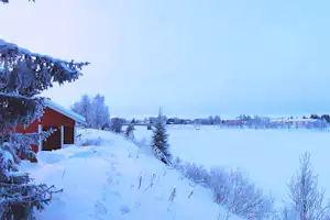 Schneebedeckte Landschaft mit Holzgebäude, verschneiten Wegen und Bäumen auf dem Campingplatz.