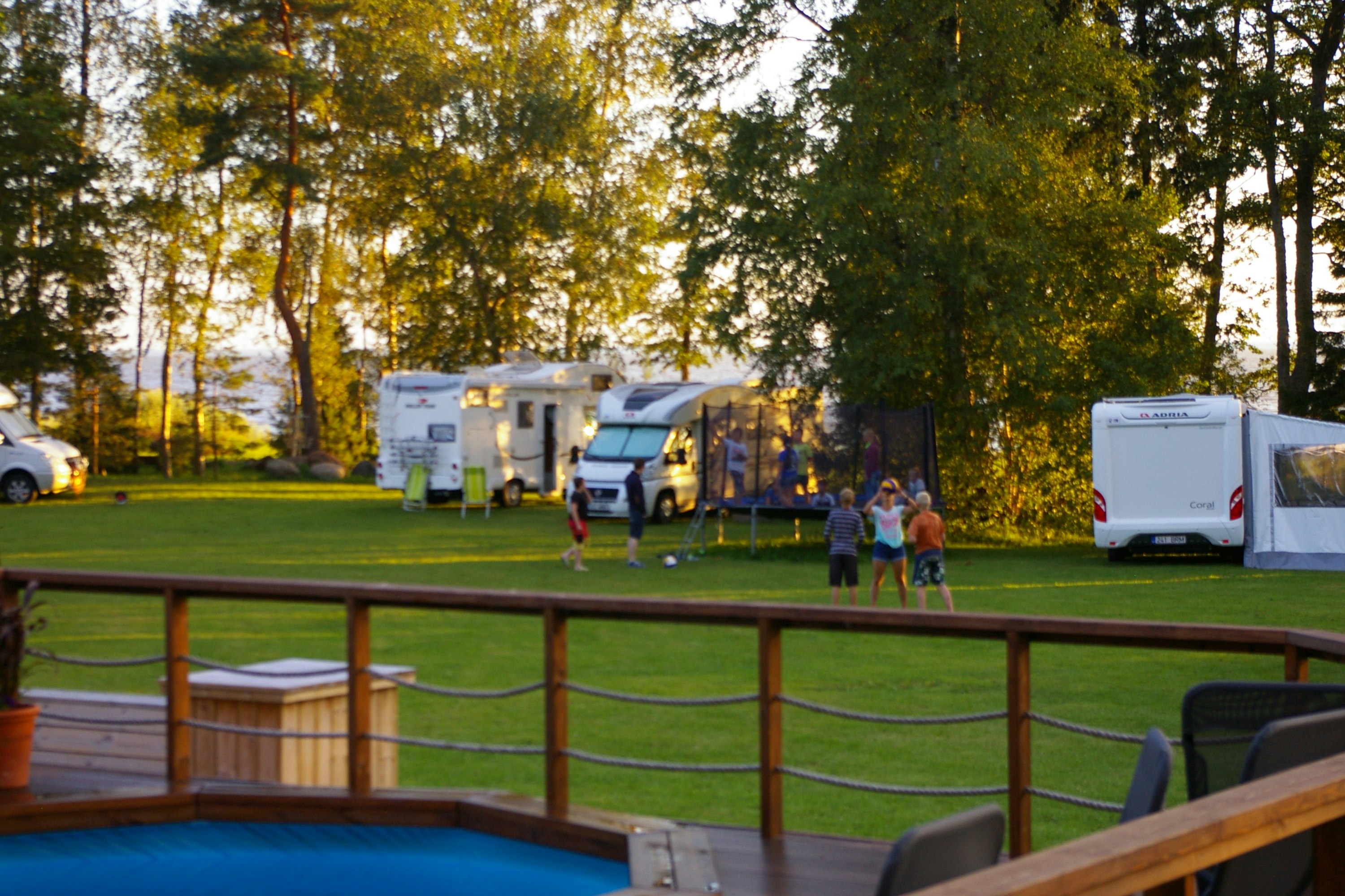 Kiviranna Holiday Home - Pool im Vordergrund, spielende Kinder auf der Wiese und Wohnwagen zwischen Bäumen im Hintergrund
