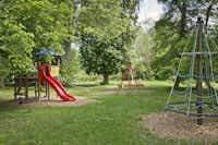 KNAUS Campingpark Frickenhausen - der Spielplatz mit mehreren Spielgeräten auf einer Wiese mit schattenspendenden Bäumen
