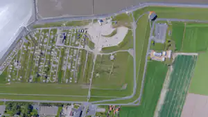 Luftaufnahme einer Campinganlage mit vielen Stellplätzen, Wegen, Grünflächen und mehreren Gebäuden im Hintergrund.