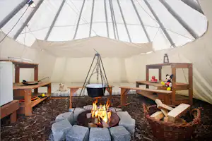 KNAUS Campingpark Viechtach - Innenansicht eine Tipis mit Feuerstelle, Sitzmöbeln und Matratzenlager