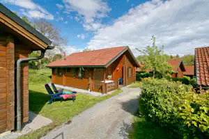 KNAUS Campingpark Viechtach - feststehende Ferienhäuser mit Terrasse an einem gekiesten Fußweg auf einer Wiese