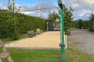 Terrasse mit Sitzgarnitur auf Kiesweg, grüner Rasen und Hecken am Campingplatz, im Hintergrund Bäume und Himmel.