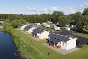 Campingplatz am Fluss mit Mobilheimen, gepflasterten Wegen, Rasenflächen und Bäumen entlang des Ufers.
