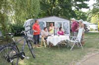 Komfortcamping Senftenberger See - Gäste vor dem Wohnwagen im Schatten unter Bäumen auf dem Campingplatz