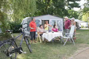 Komfortcamping Senftenberger See - Gäste vor dem Wohnwagen im Schatten unter Bäumen auf dem Campingplatz