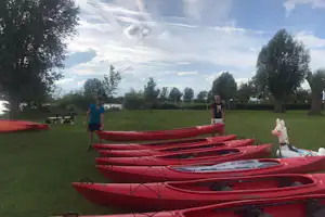 Rote Kanus auf grünem Rasen, im Hintergrund Bäume und zwei Personen am Campingplatz.