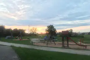 Spielplatz auf dem Campingplatz mit Rutsche und Schaukeln, Rasenfläche und Wegen, im Hintergrund Bäume und Abendhimmel.