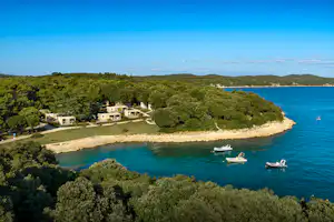 Blick auf eine Küstenbucht mit Campingplatz, Wohnwagen und Booten im Wasser, umgeben von grünen Hügeln und Bäumen.