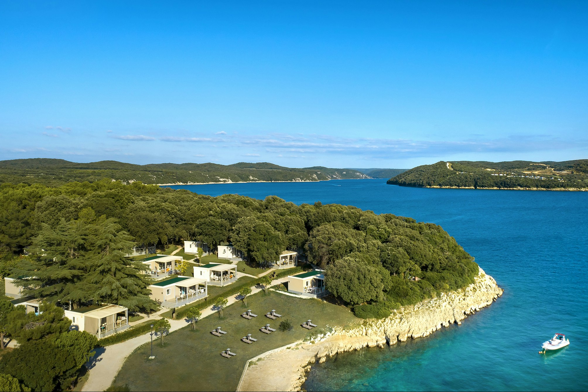 Campinganlage an einer Bucht mit Küste, weißen Gebäuden, Stellplätzen und Blick aufs Meer und die Inseln.