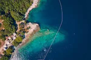 Luftaufnahme einer türkisfarbenen Bucht mit Strandabschnitten, Booten und einem kleinen Campingbereich am Ufer.