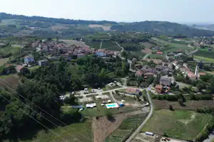 Luftaufnahme eines Campingplatzes im Tal mit Wohnhäusern, Wegen, Grünflächen und mehreren Stellplätzen am Hang.