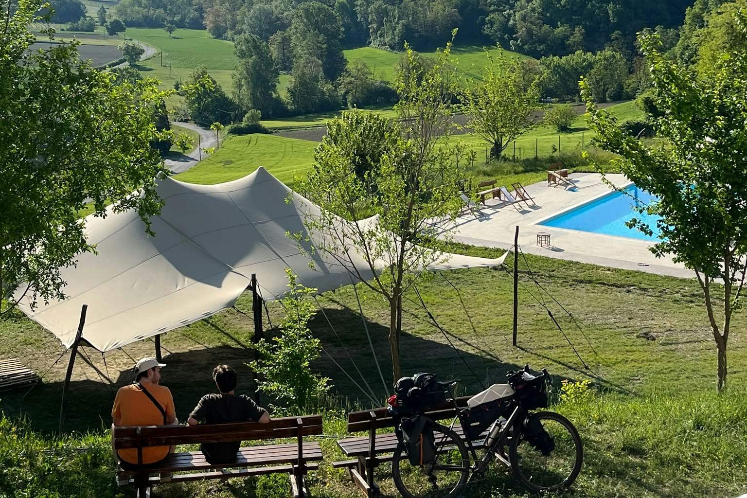 Zelt auf einem Campingplatz mit Blick auf grüne Hügel, Bäume und einen kleinen Pool im Hintergrund.
