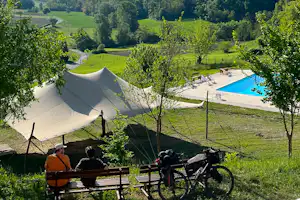 Zelt auf einem Campingplatz mit Blick auf grüne Hügel, Bäume und einen kleinen Pool im Hintergrund.