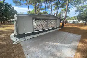 Campingzelt mit Vorraum auf Stellplatz, am Boden eine Plane, umgeben von Bäumen im Wald.