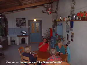 Terrasse am Haus La Grande Curtille: gedeckter Tisch, mehrere Personen sitzen beim Abendessen, Holzdecke und Blumen im Hintergrund.
