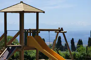 Spielplatz mit Rutsche und Holzgerüst, Blick auf Berge und weite Landschaft im Hintergrund.