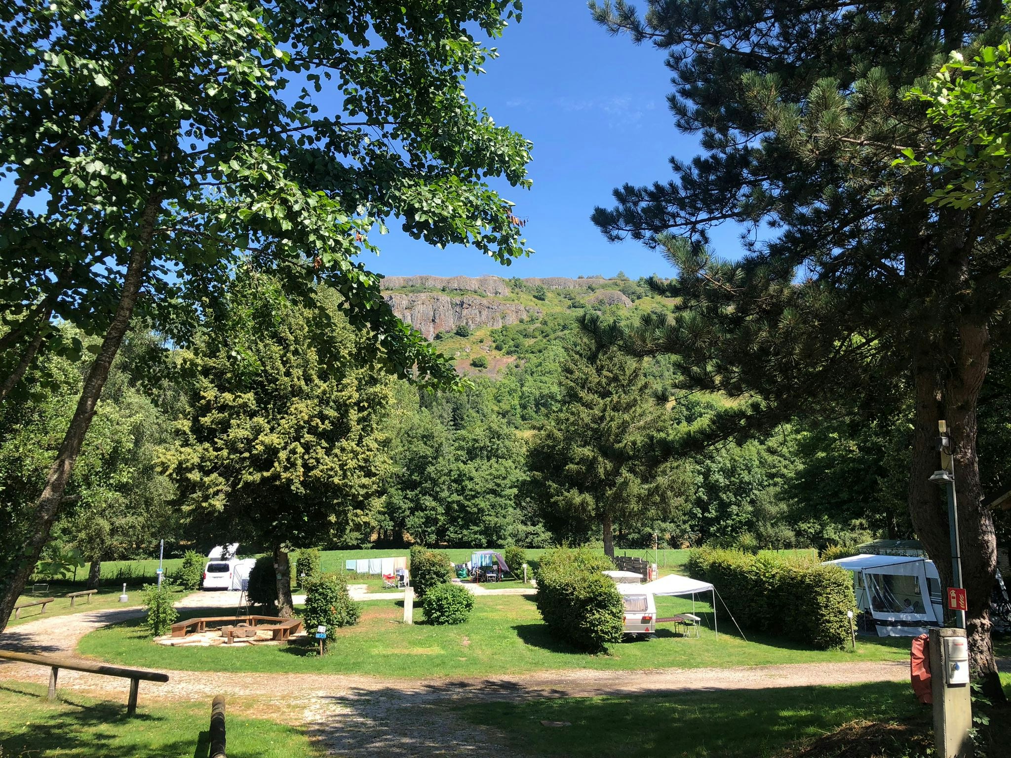 Campingplatz im Grünen mit mehreren Wohnwagen auf Stellplätzen, umgeben von Bäumen und Rasenflächen.