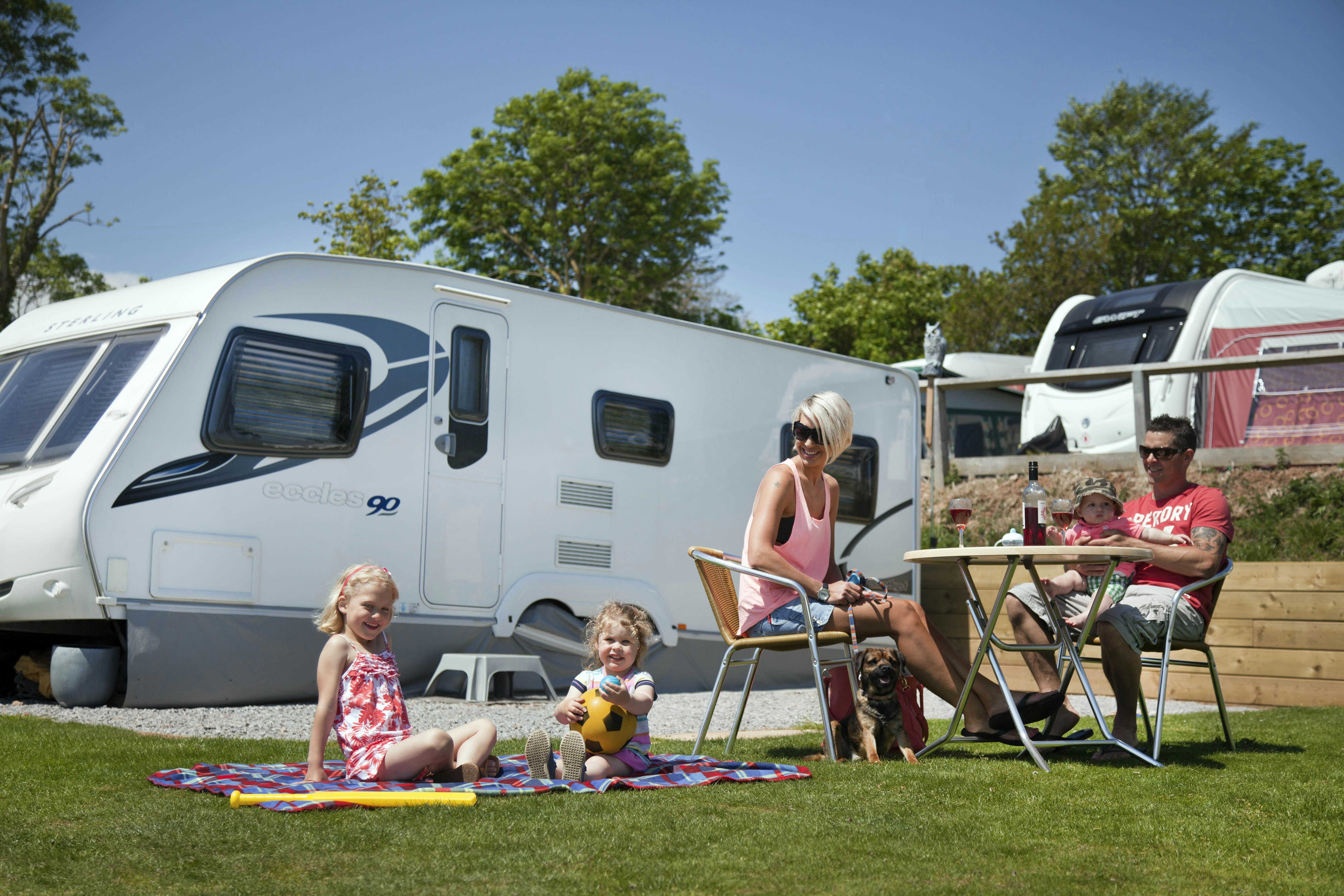 Ladram Bay Holiday Park - Familie sitzt vor ihrem Wohnwagen auf einem Standplatz