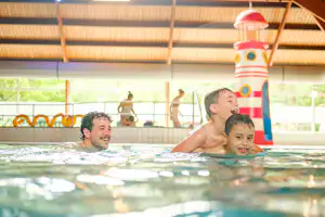 Familie im Schwimmbecken, Kinder und Erwachsene im Wasser, bunte Wasserrutsche im Hintergrund.