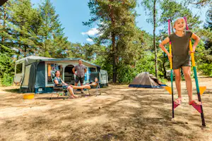 Familie im Campinglager: Zelt, Campingstühle und Tisch auf dem Stellplatz zwischen hohen Bäumen.