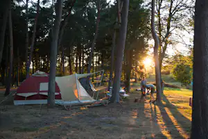 Campingzelt im Wald, Sonnenuntergang durch Bäume, Picknicktisch und Stühle am Stellplatz.