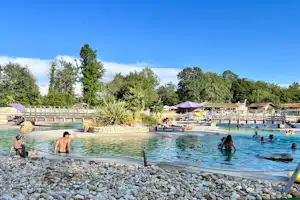 Schwimmbecken im Campingbereich mit Sonnenschirmen, Liegen und Steinen am Beckenrand, umgeben von Bäumen.