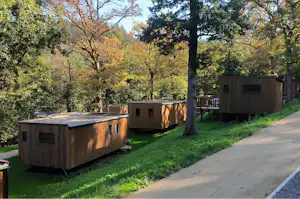 Holz-Mobilheime auf Stelzen am Campingplatz, mit Rasen, gepflastertem Weg und Bäumen im Hintergrund.