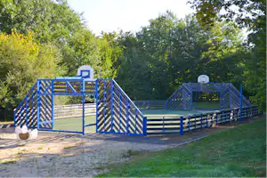 Blauer umzäunter Campingplatz mit mehreren Stellflächen, Holzstufen und einem kleinen Schild, umgeben von Bäumen im Hintergrund.