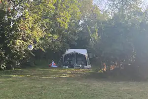 Campingzelt mit Vorzelt und Lichterkette auf einer Wiese, umgeben von Bäumen im Hintergrund.