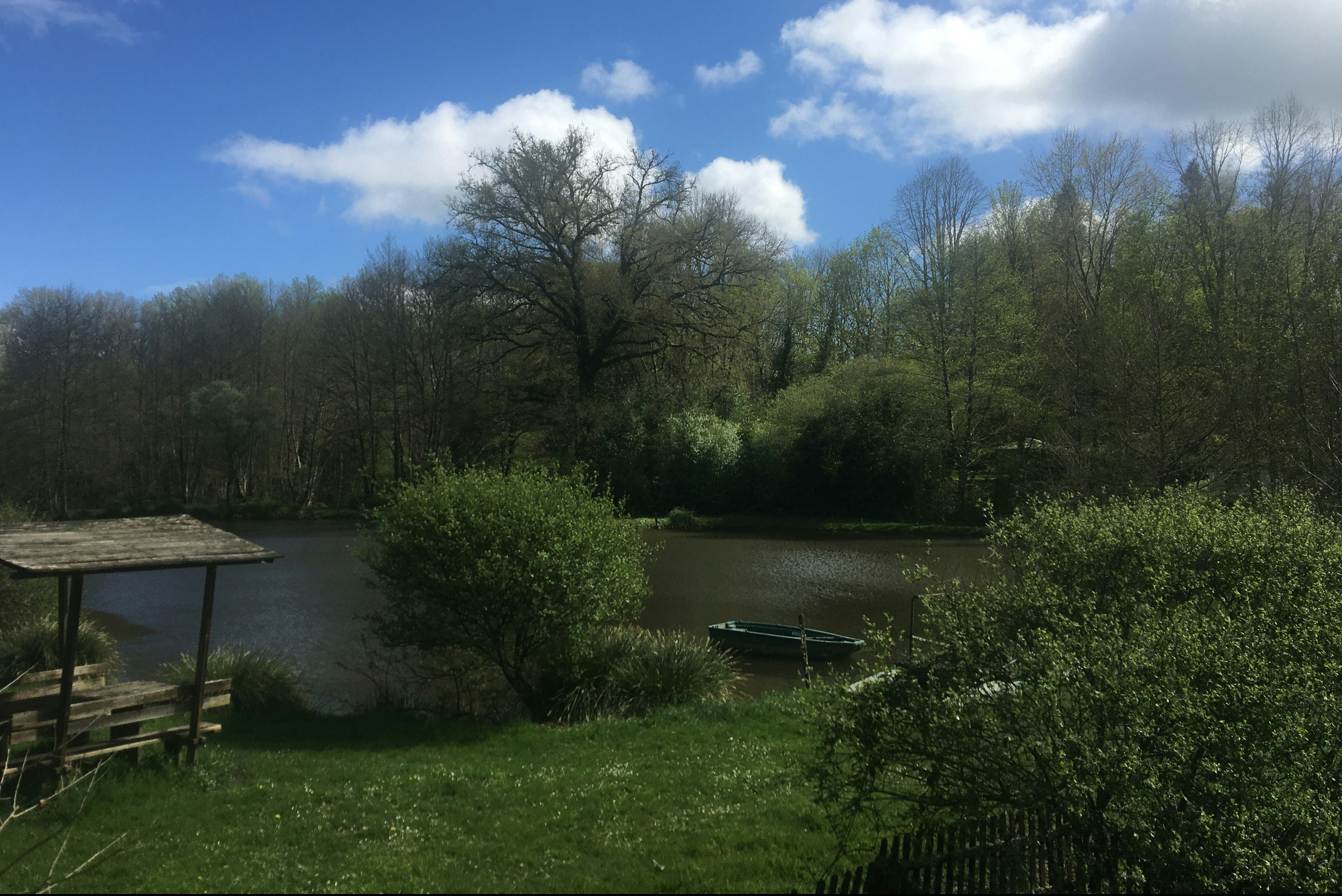 Blick auf einen Camping-See mit Ruderboot am Ufer, umgeben von Bäumen und einem Steg.