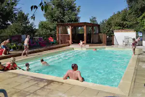 Schwimmbecken auf dem Campingplatz mit Holzpavillon, Liegestühlen und bunten Gartenstühlen im Hintergrund.