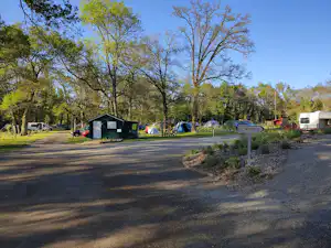 Campingplatz mit breitem Weg, Zelte und Wohnwagen am Rand, Bäume und Sträucher im Hintergrund.